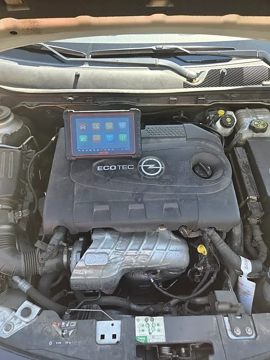 Tester Autel MK900-BT leżący na pokrywie silnika Opel Ecotec podczas odczytu błędów, widoczne menu urządzenia