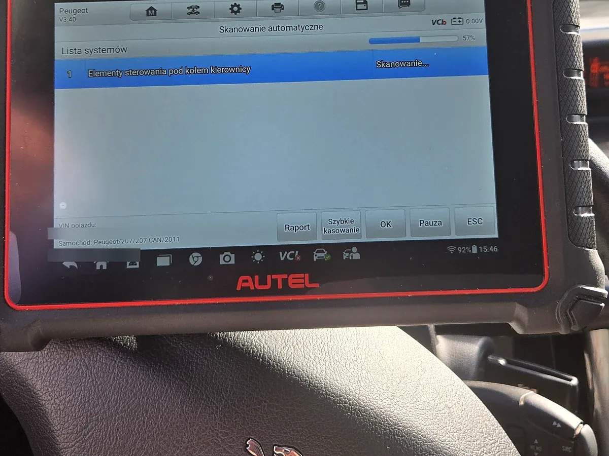 Tester Autel MaxiCOM MK900-BT na kolumnie kierownicy Peugeota 207, na ekranie skanowanie automatyczne 57 procent i lista systemów, u dołu widoczne logo Peugeot na poduszce kierownicy