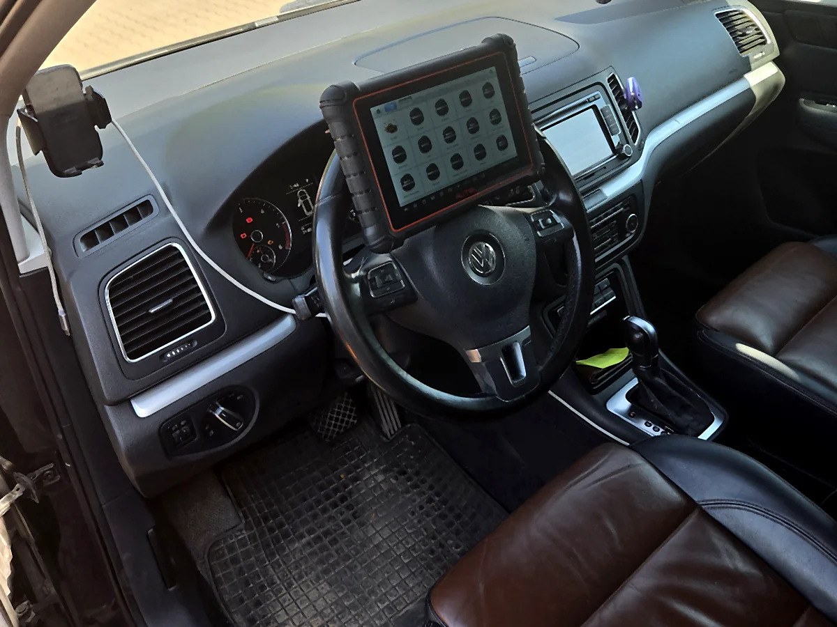 Wnętrze VW Sharana 7N od strony kierowcy z brązową skórzaną tapicerką, tester Autel MaxiCOM MK900-BT oparty o kierownicę z otwartym menu wyboru marek, w konsoli środkowej dźwignia skrzyni automatycznej DSG